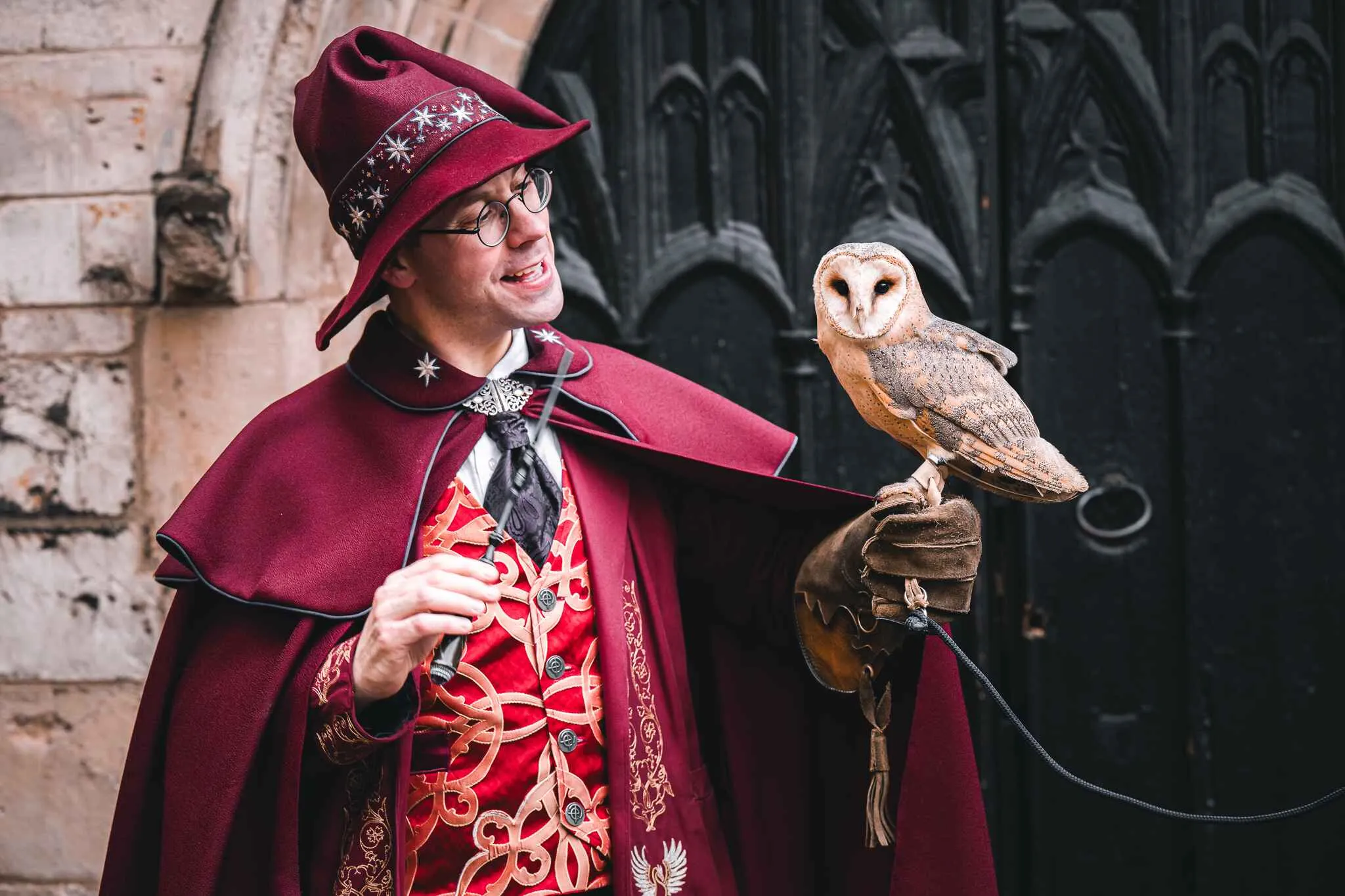 Wizard of York in his red cape holding a wand in his right hand and with an owl perched on his left hand.